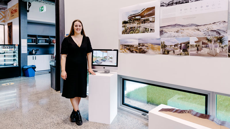 Master of Architecture student beside drawings, models and digital visualisations in an exhibition space